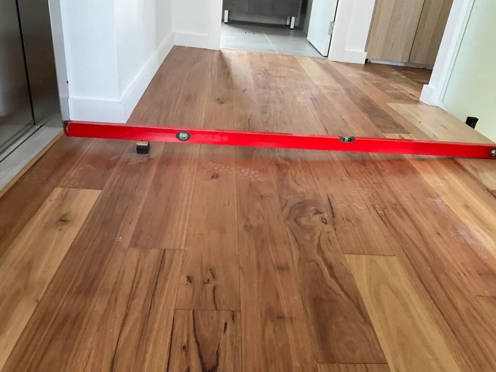 Building inspector checking an uneven floor with a level during a handover inspection.